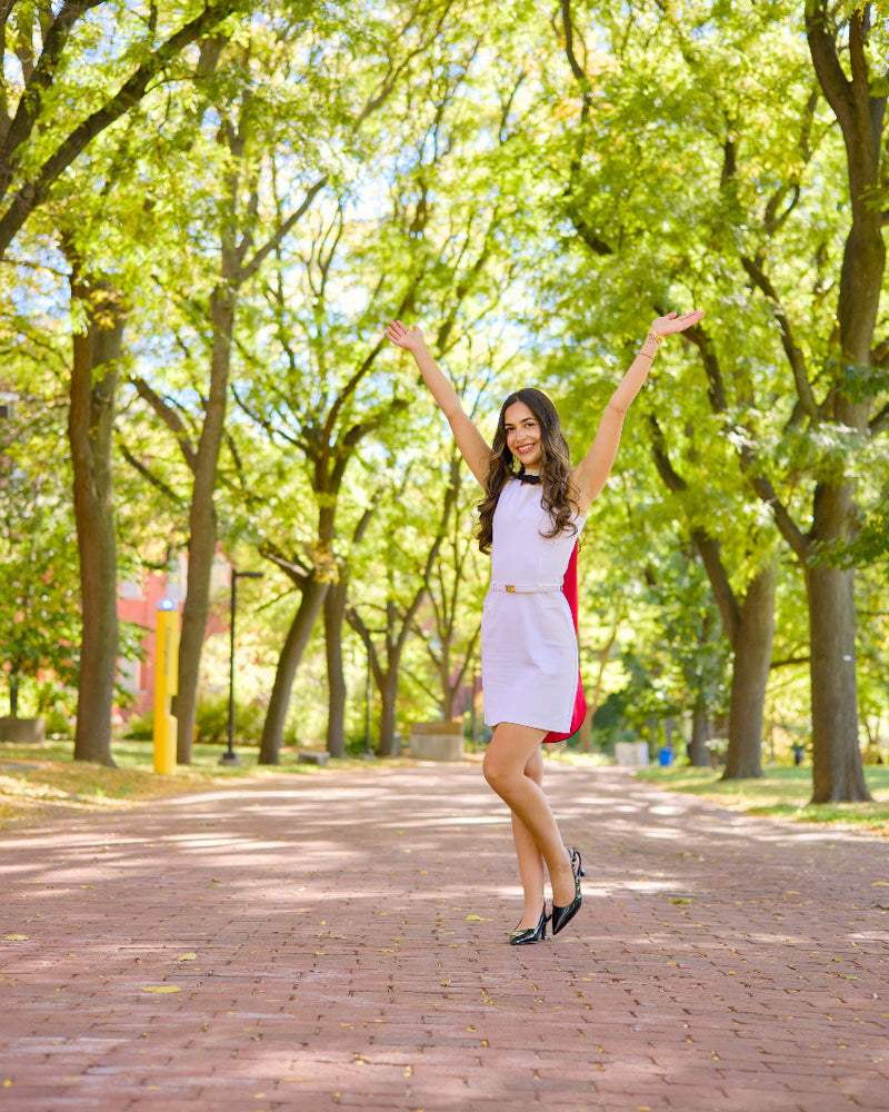 A professional photo of a Guelph grad on the University of Guelph campus, The Woman in a white dress with red accents standing on Alumni Walk pathway, the photo is from Guelph Grad Photos. The background is the Alumni Walk on the University of Guelph Campus.