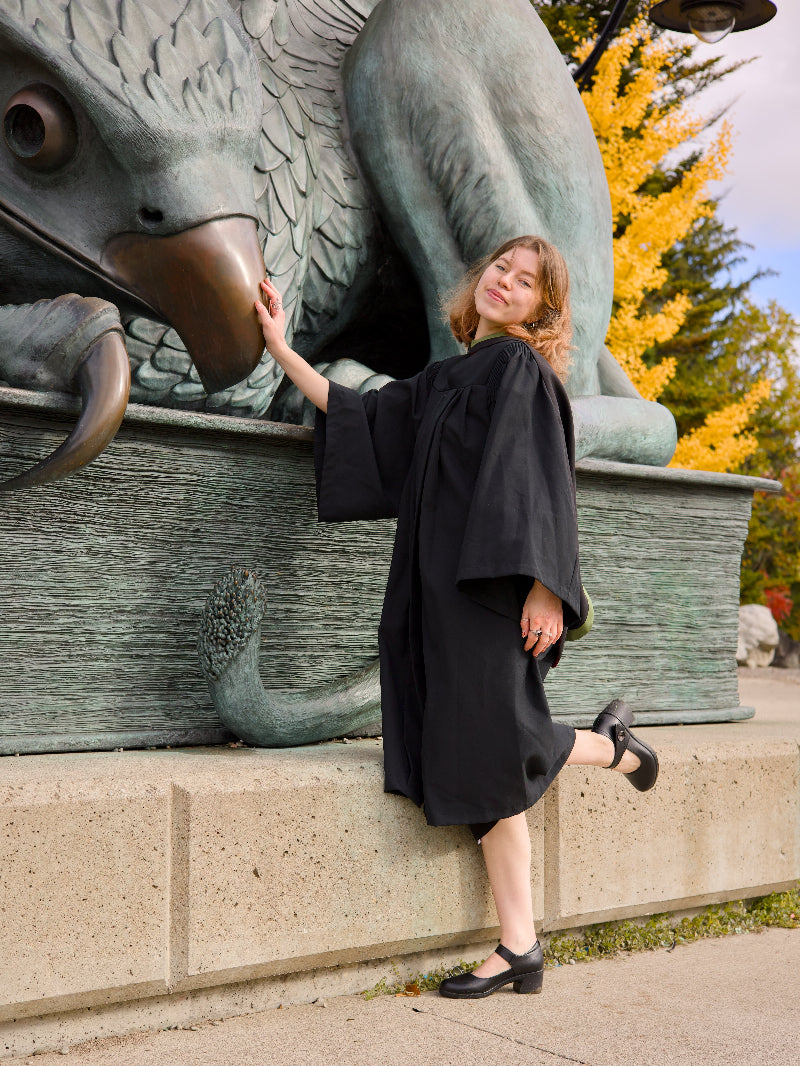 A woman in a graduation gown sitting on the Guelph Gryphon sculpture on Campus