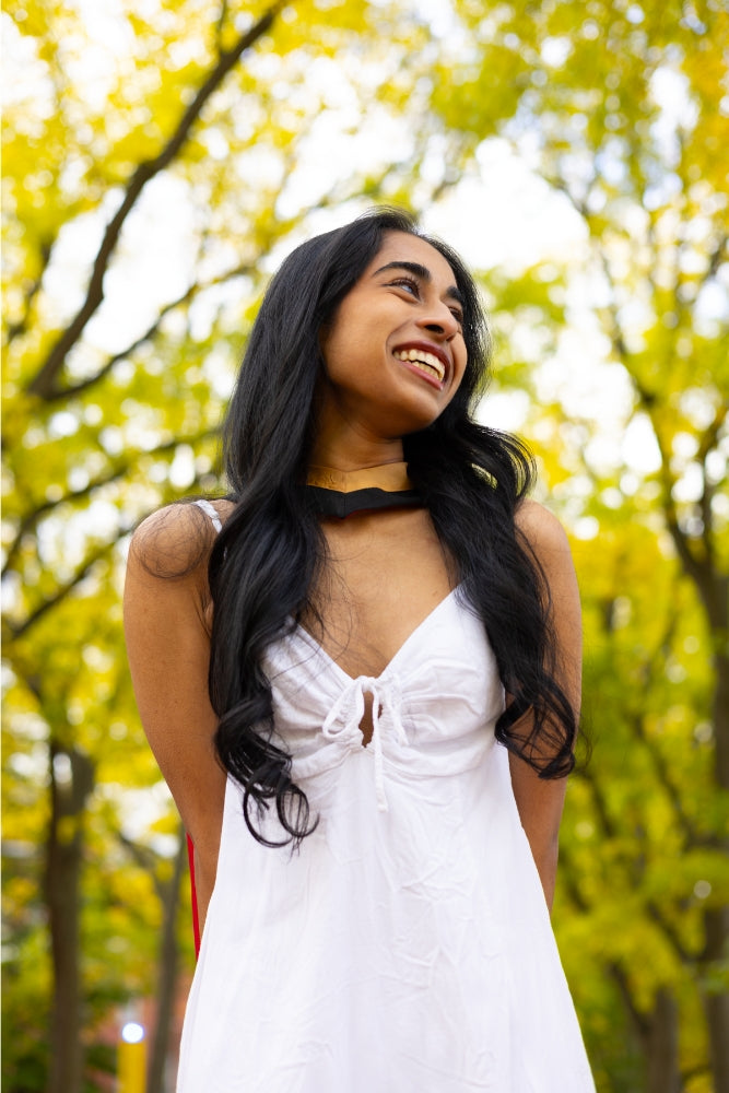 A young woman in a white dress, on Alumni Walk Tree-Lined Path on the University of Guelph Campus, with autumn trees in the background. The photo is from Guelph Grad Photos. 