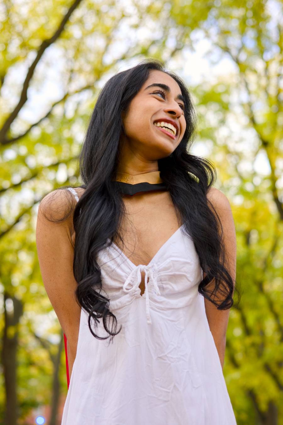 Woman in a white dress standing outdoors with greenery in the background. The photo is from Guelph Grad Photos. The background is the University of Guelph Campus.
