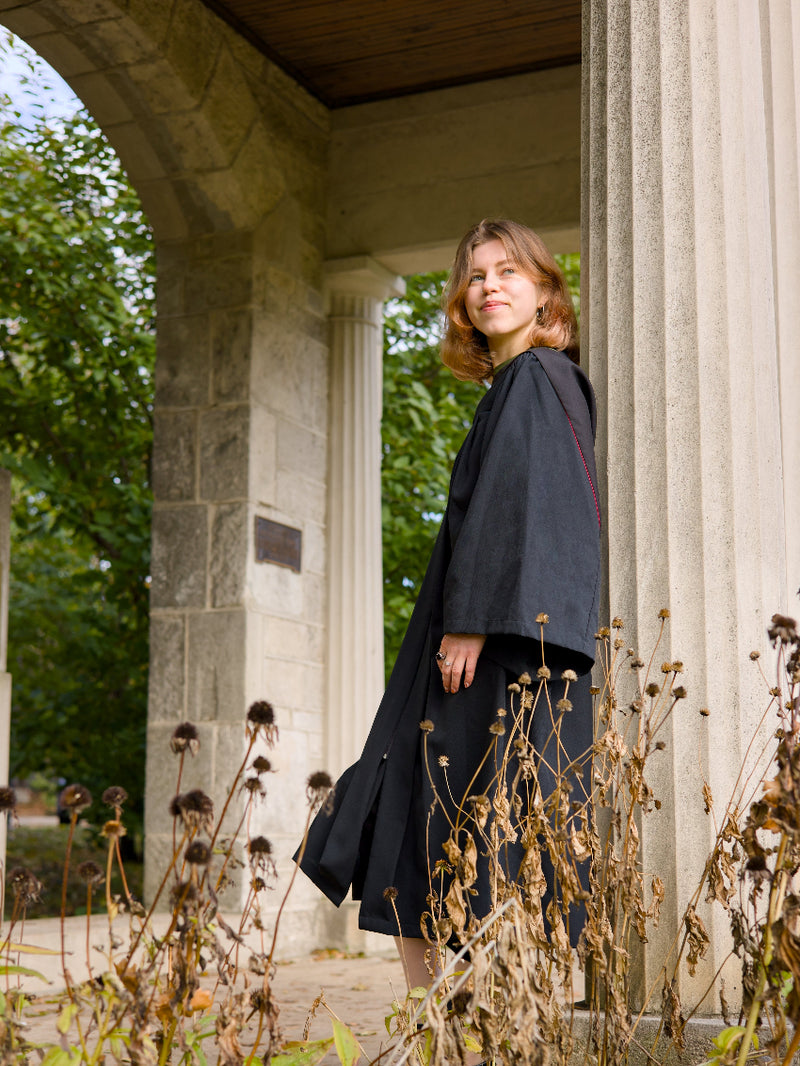Woman standing in a stone archway with greenery around. The photo is from Guelph Grad Photos. The background is the University of Guelph Campus.