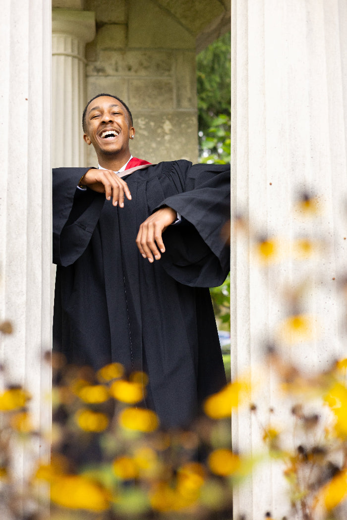 Graduate in cap and gown standing outdoors with flowers in the foreground.The photo is from Guelph Grad Photos. The background is the University of Guelph Campus.