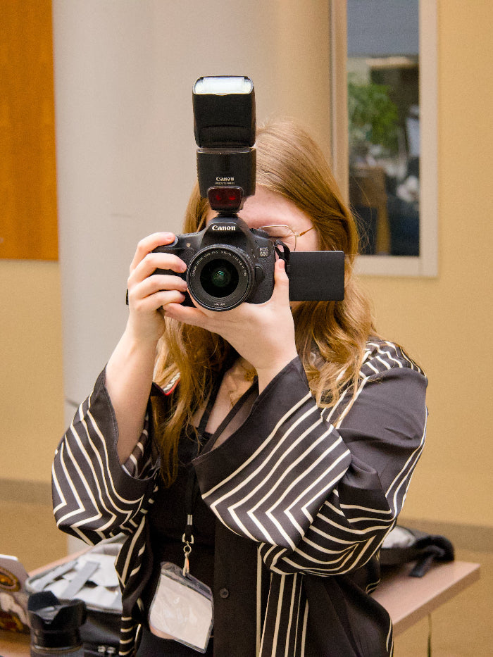 Guelph Grad Photographer holding a Canon camera up to their face in an indoor setting