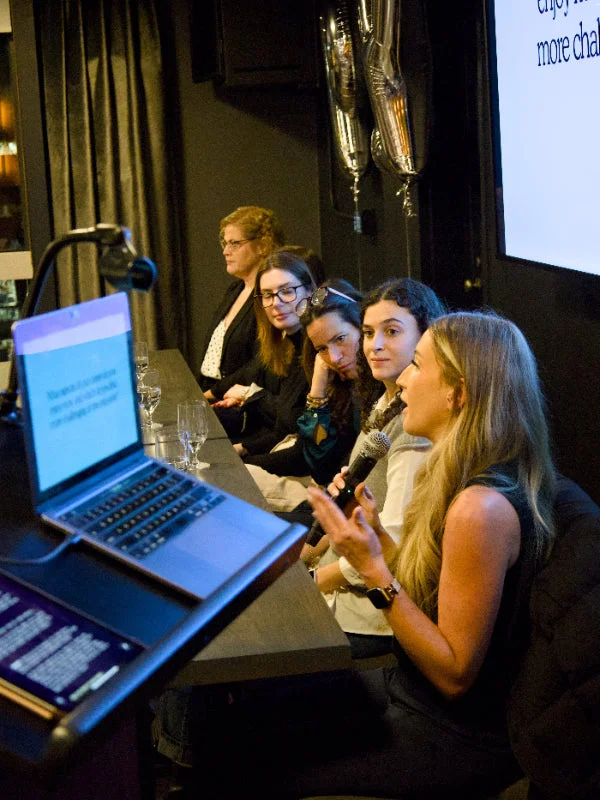 Group of people seated at round tables in a large room with a speaker at a podium during a university event at the University of Guelph.