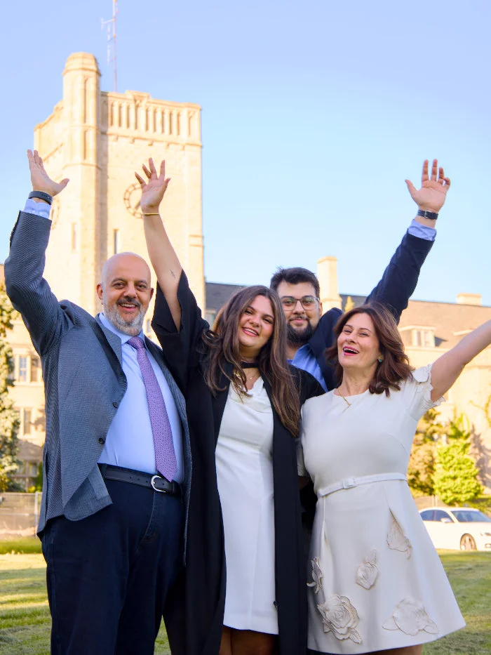 Four people with arms raised in front of the Johnston Clock Tower on the University of Guelph campus