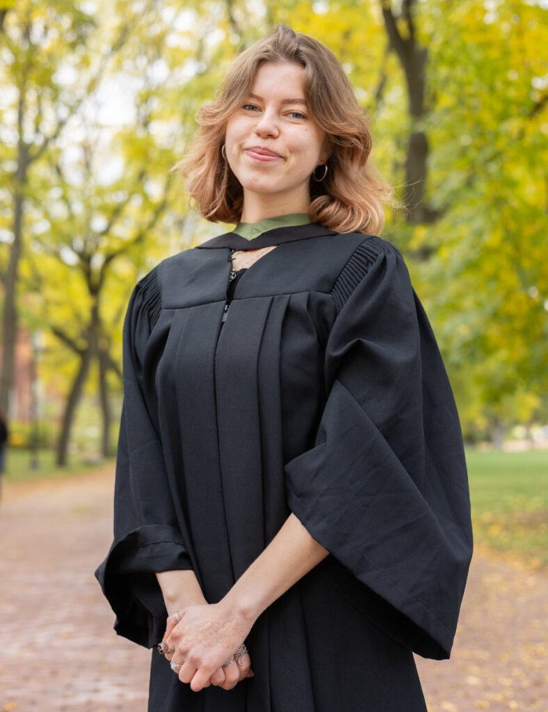 A professional photo of a young woman in a graduation gown. sitting on the Gryphon Statue on the University of Guelph Campus. The photo is from Guelph Grad Photos.