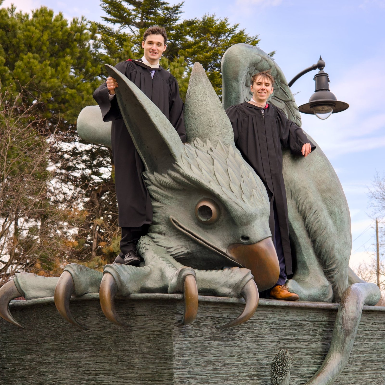 two young grads in a graduation gown sitting on the Guelph Gryphon sculpture on Campus