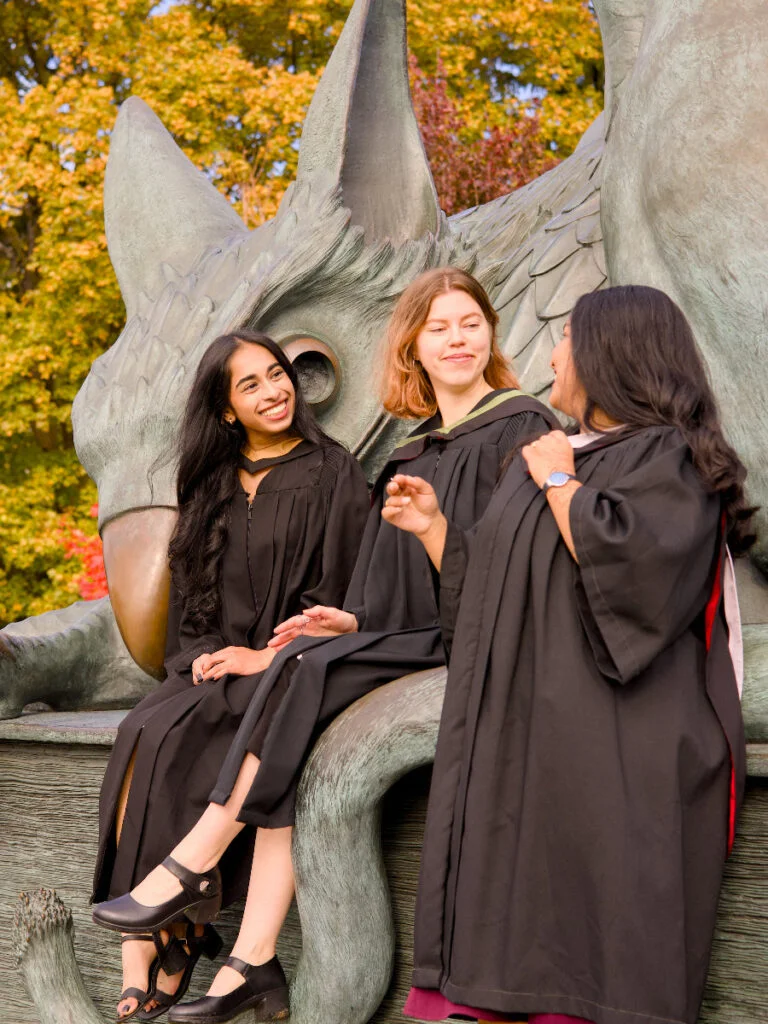 A professional photo of three young Guelph grads on the University of Guelph campus in graduation gowns, posing in front of the University of Guelph sign. The photo is from Guelph Grad Photos. The background is the Gryphon Statue on the University of Guelph Campus.