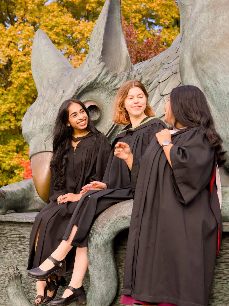 A professional photo of three young Guelph grads on the University of Guelph campus in graduation gowns, posing in front of the University of Guelph sign. The photo is from Guelph Grad Photos. The background is the Gryphon Statue on the University of Guelph Campus.