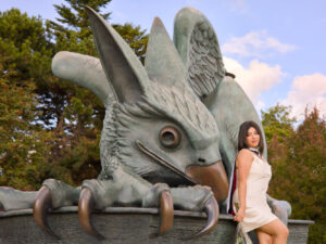 Woman posing with a large, green, dragon-like creature statue outdoors.