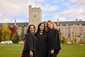 Three individuals in graduation gowns standing on a grassy area with a building in the background