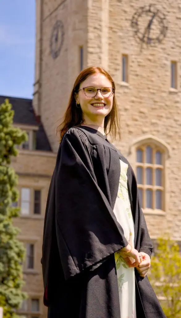 Person in graduation gown standing in front of a clock tower. The photo is from Guelph Grad Photos. The background is the University of Guelph Campus.