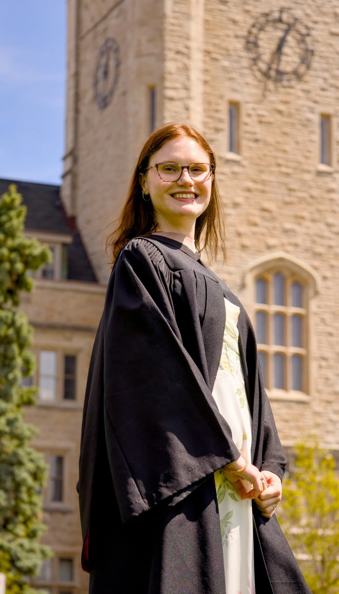 Person in graduation gown standing in front of a clock tower. The photo is from Guelph Grad Photos. The background is the University of Guelph Campus.