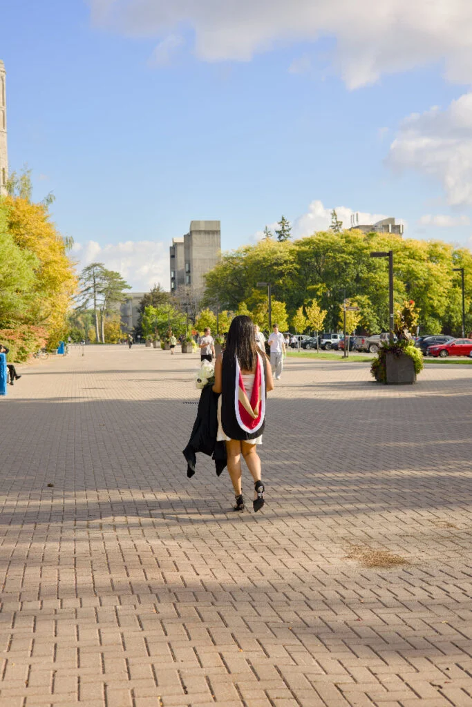 Person walking on a paved path with trees and buildings in the background