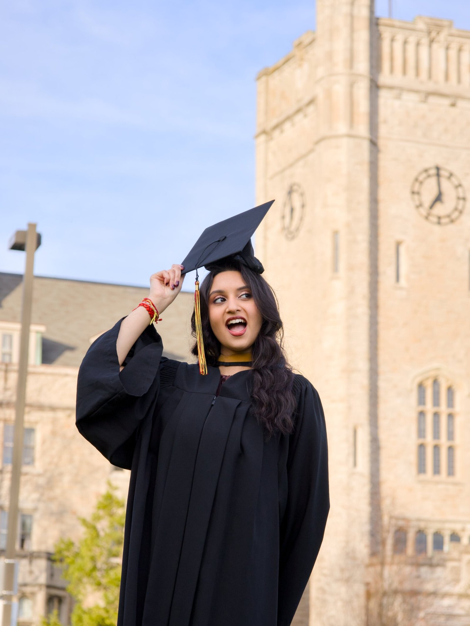 Graduate in black cap and gown posing in front of a clock tower. The photo is from Guelph Grad Photos. The background is the University of Guelph Campus.