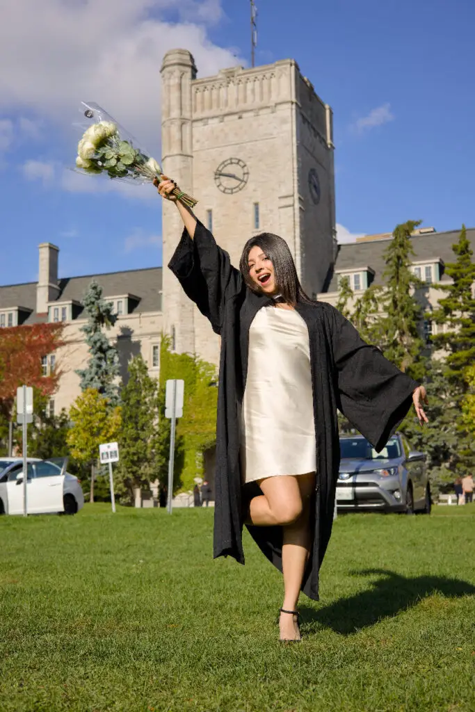 Graduate in cap and gown celebrating outdoors with a clock tower in the background