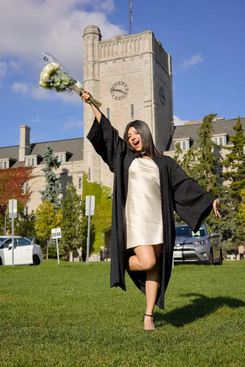 Graduate in cap and gown celebrating outdoors with a clock tower in the background