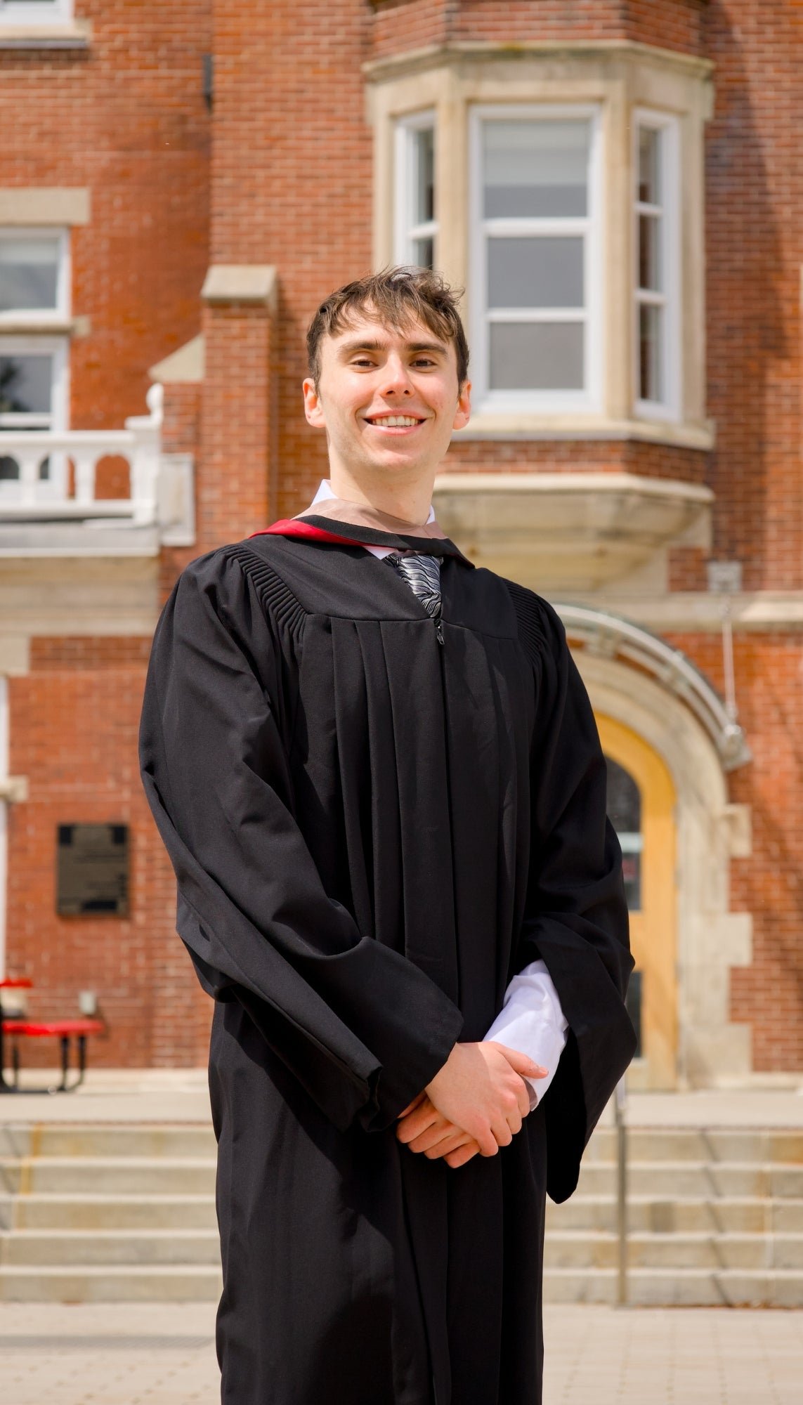 A professional photo of a Guelph grad on the University of Guelph campus. Graduate in a black gown standing in front of the LANG Building.