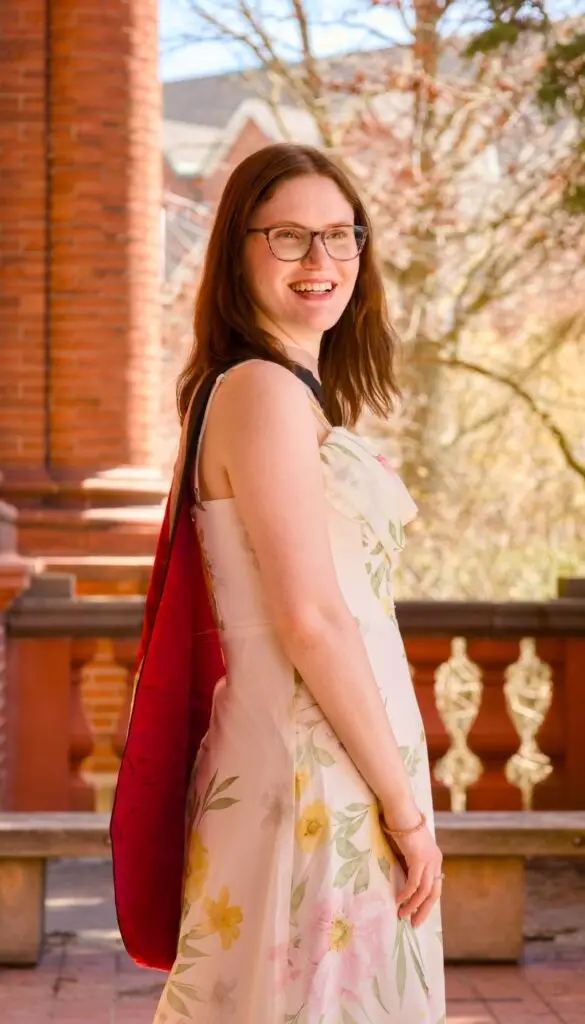 Woman wearing glasses and a floral dress with a red bag outdoors. The photo is from Guelph Grad Photos. The background is the University of Guelph Campus.