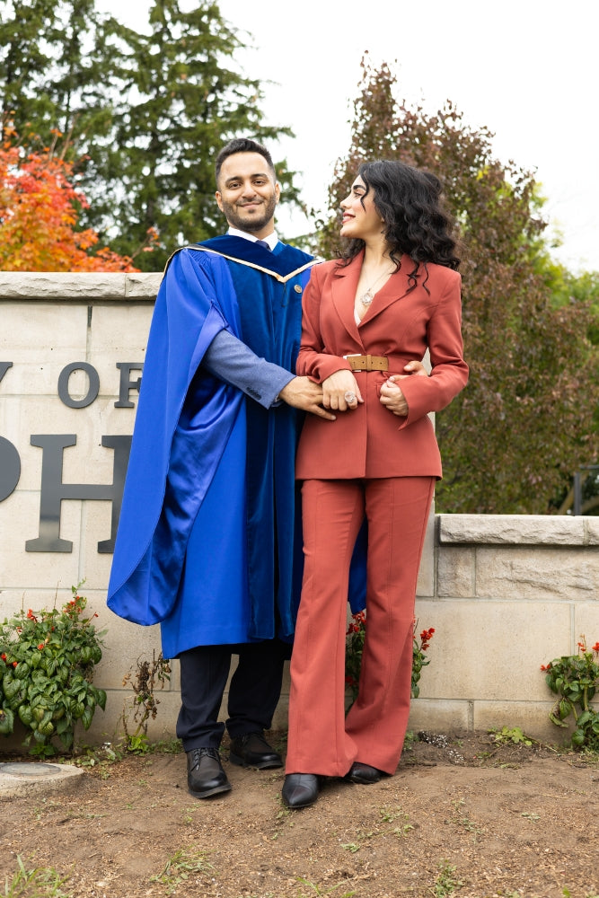 Person in blue graduation gown and cap standing next to another person in a red suit outdoors.
