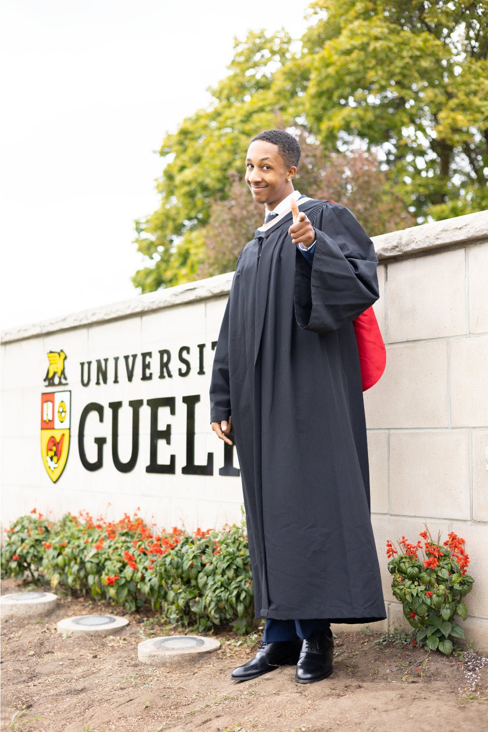 Graduate in a cap and gown standing in front of the University of Guelph sign.