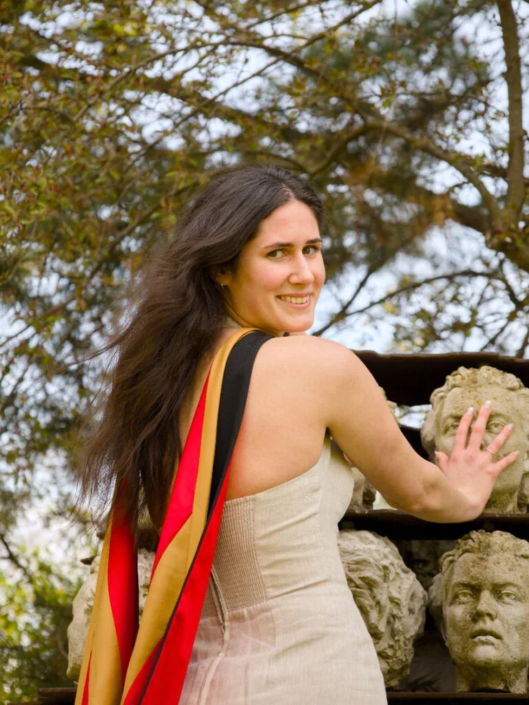 A professional photo of a Guelph grad on the University of Guelph campus , a woman with a colorful scarf standing next to stone sculptures outdoors. The photo is from Guelph Grad Photos. The background is The Portico on the University of Guelph Campus.
