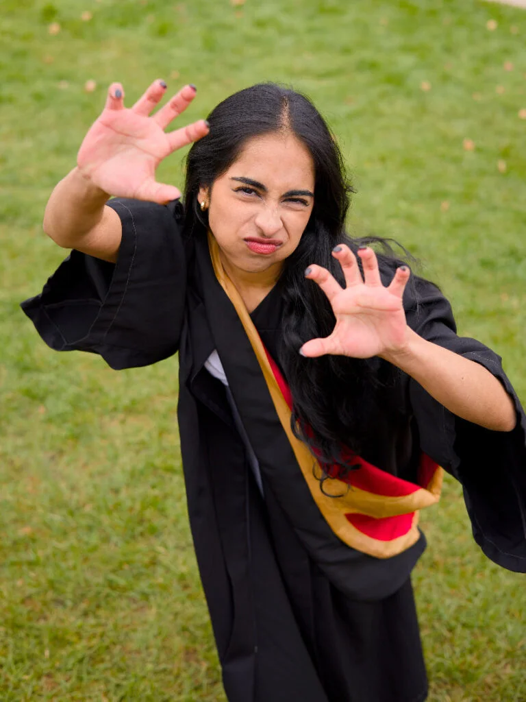 Person in a graduation gown with a colorful sash outdoors on grass,The photo is from Guelph Grad Photos. The background is the University of Guelph Campus.