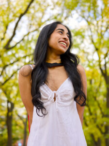 A young woman in a white dress, on Alumni Walk Tree-Lined Path on the University of Guelph Campus, with autumn trees in the background. The photo is from Guelph Grad Photos.