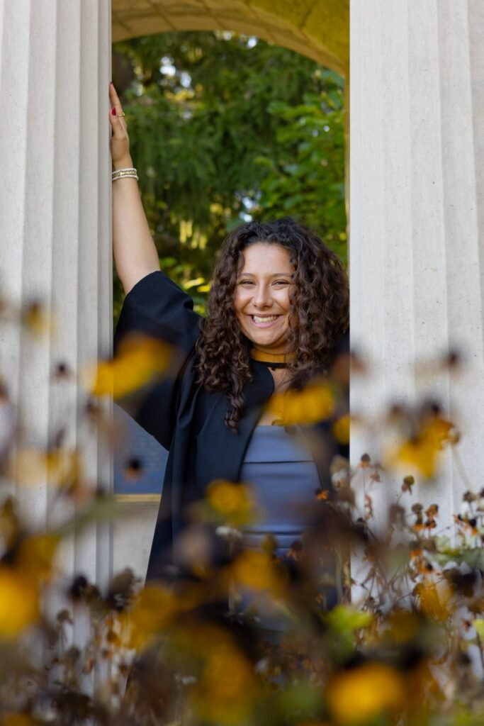 Woman standing behind a white archway with autumn leaves and flowers in the foreground