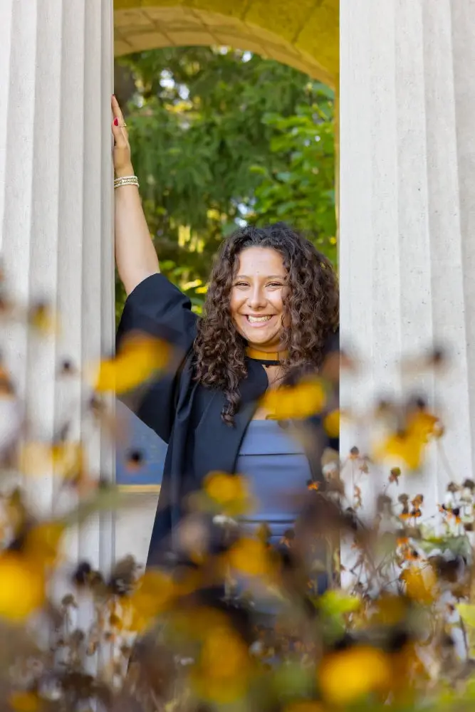A University of Guelph graduate in a graduation hood and gown standing under the stone archway of the Portico