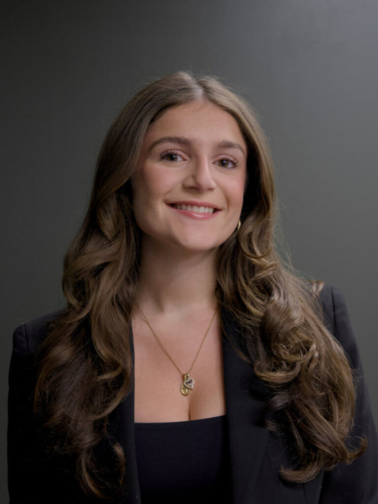 Woman with long brown hair wearing a black blazer against a gray background