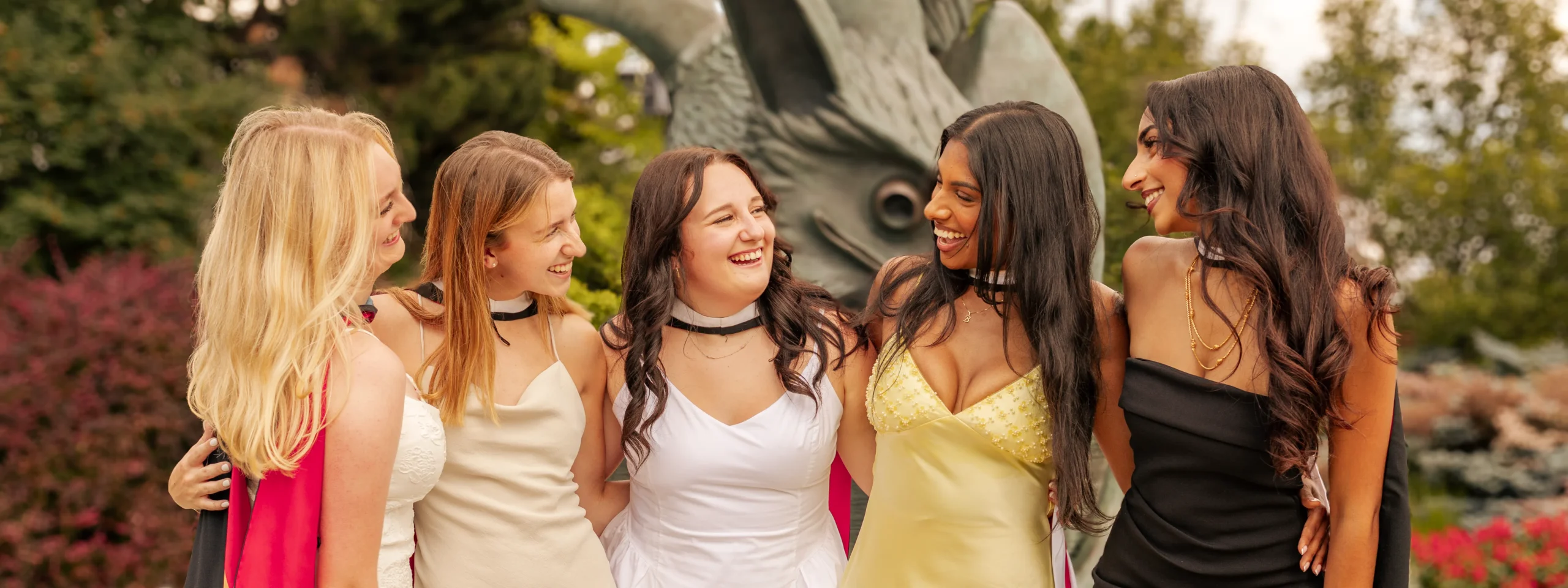 Five University of Guelph graduates laughing together in convocation stoles in front of the Gryphon statue