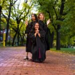 Three graduates in black gowns striking playful poses on a tree-lined brick walkway at the University of Guelph.