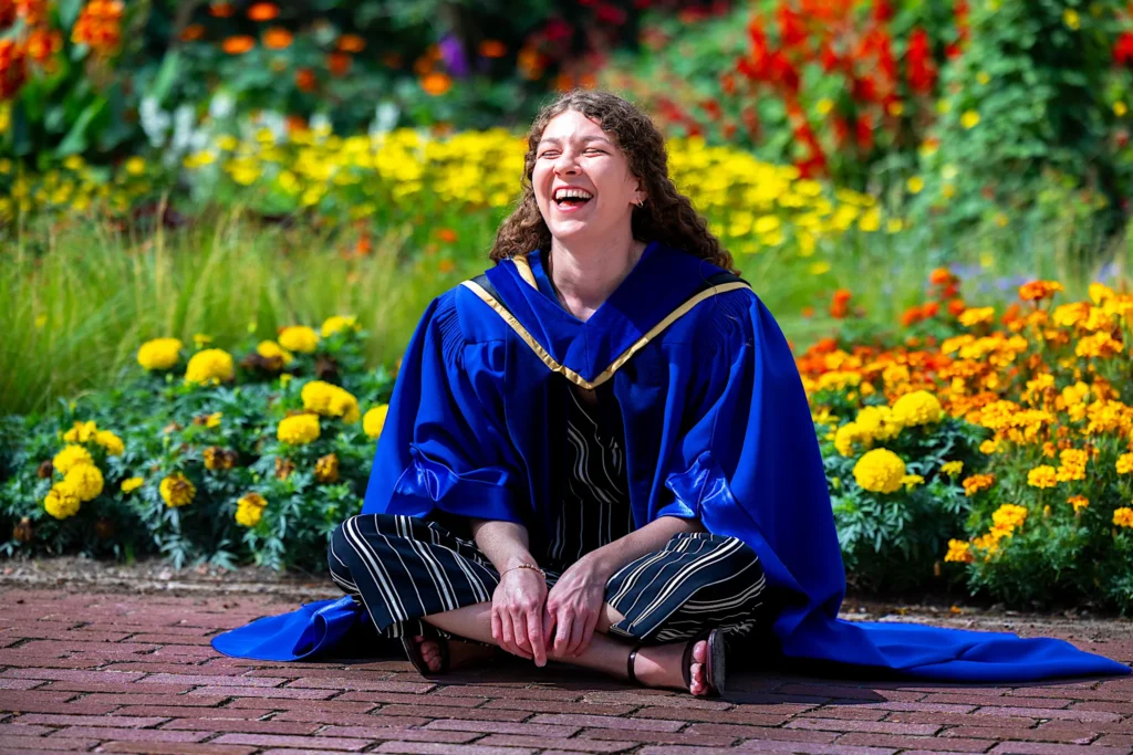 A University of Guelph graduate sitting among the marigolds in doctoral regalia.