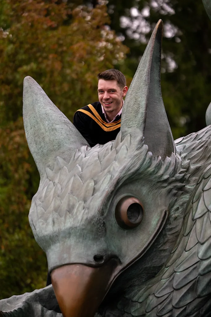 A University of Guelph graduate in regalia looking over the head of the Gryphon statue.