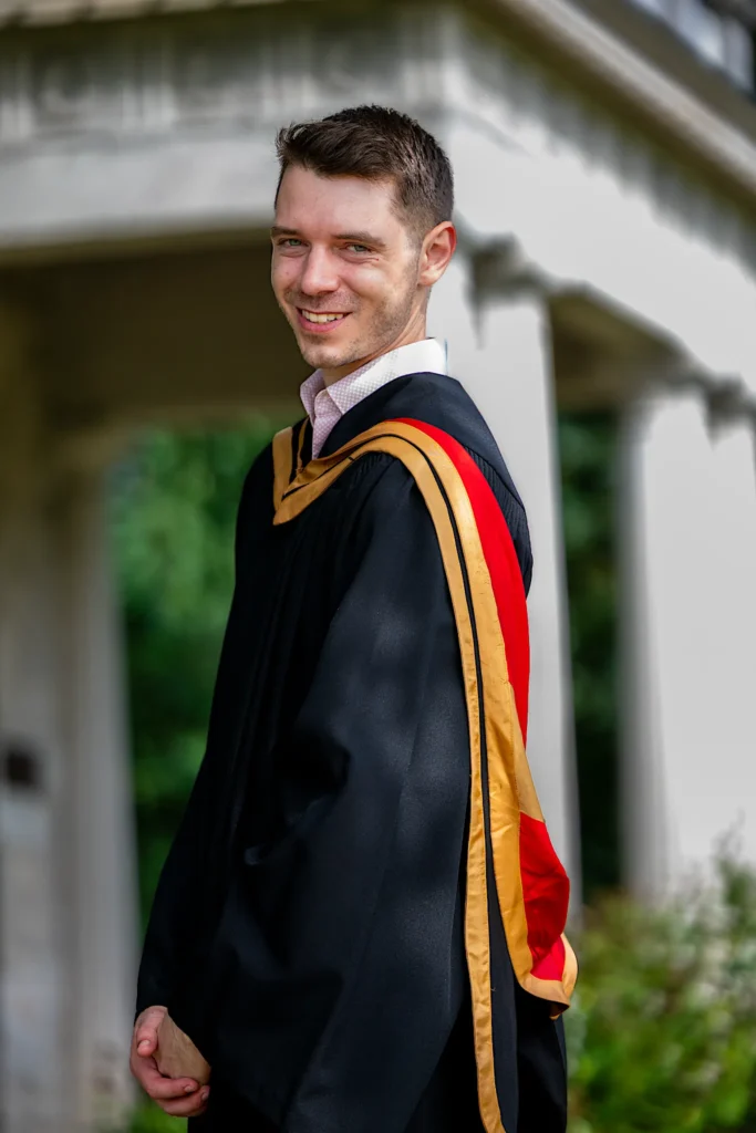 A University of Guelph graduate in regalia by the stone columns.
