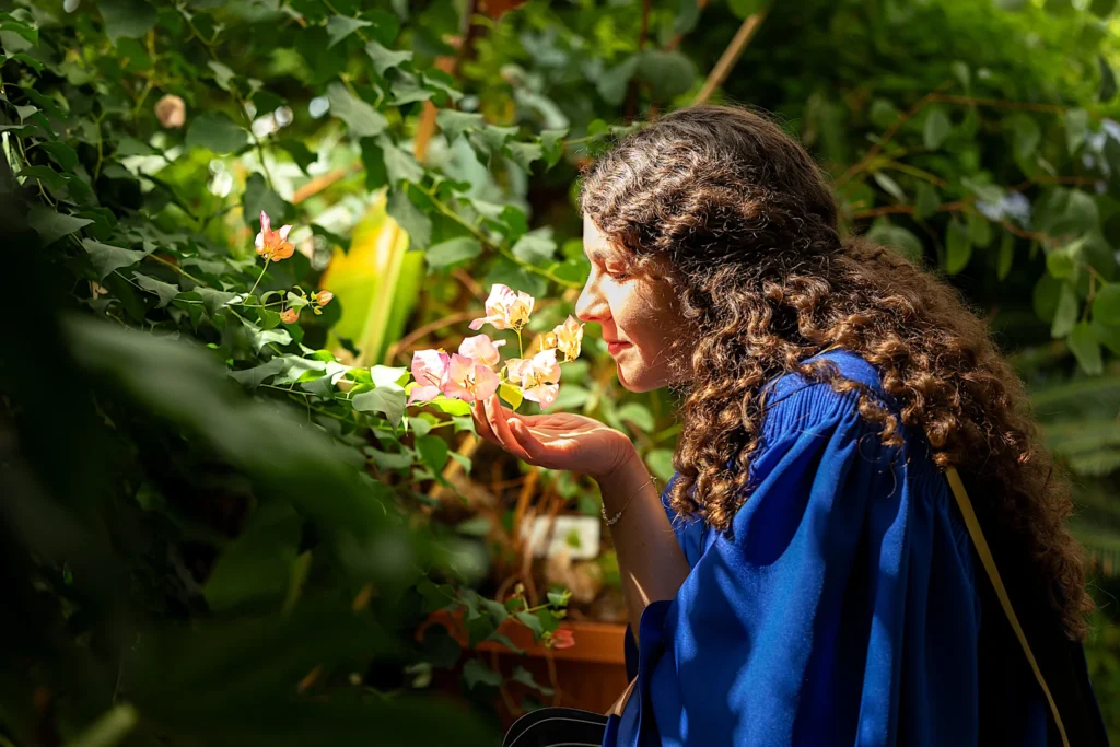 A University of Guelph graduate in regalia with a glass among the leaves.