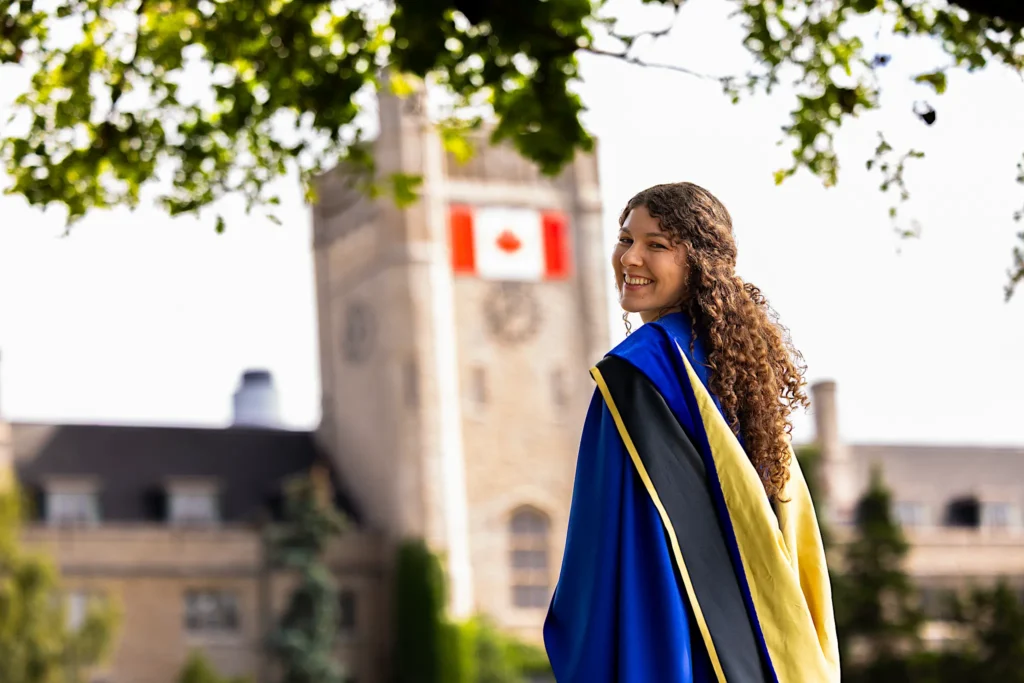 A University of Guelph graduate in doctoral regalia with the clock tower behind.