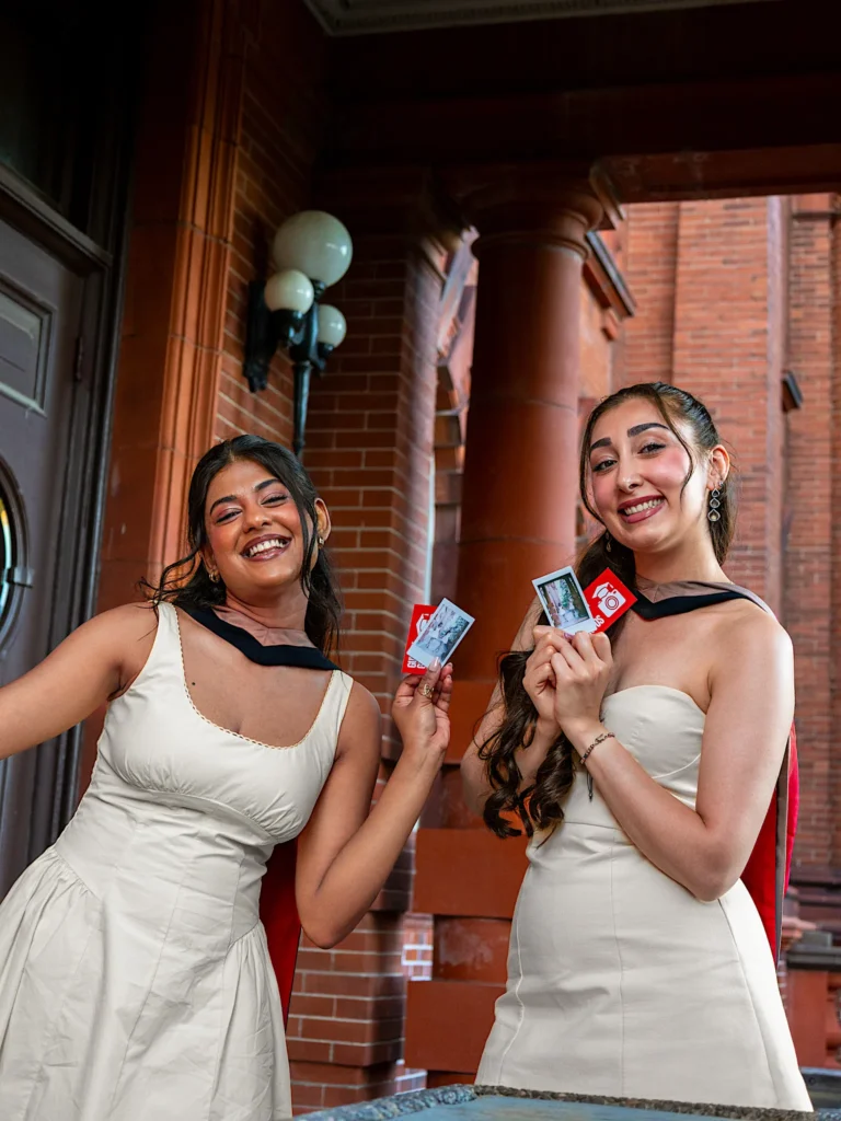 Two University of Guelph graduates laughing with their student ID cards.
