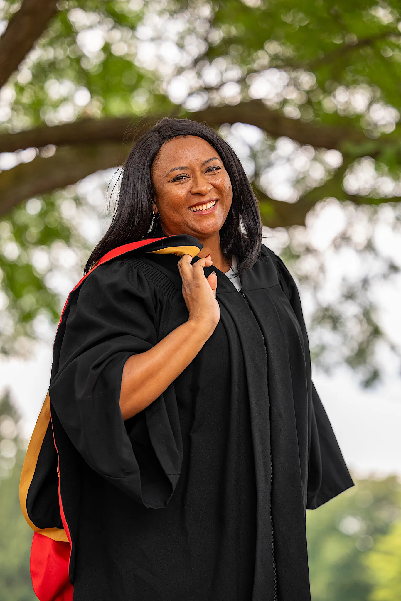 A University of Guelph graduate in regalia holding her cap under a tree.