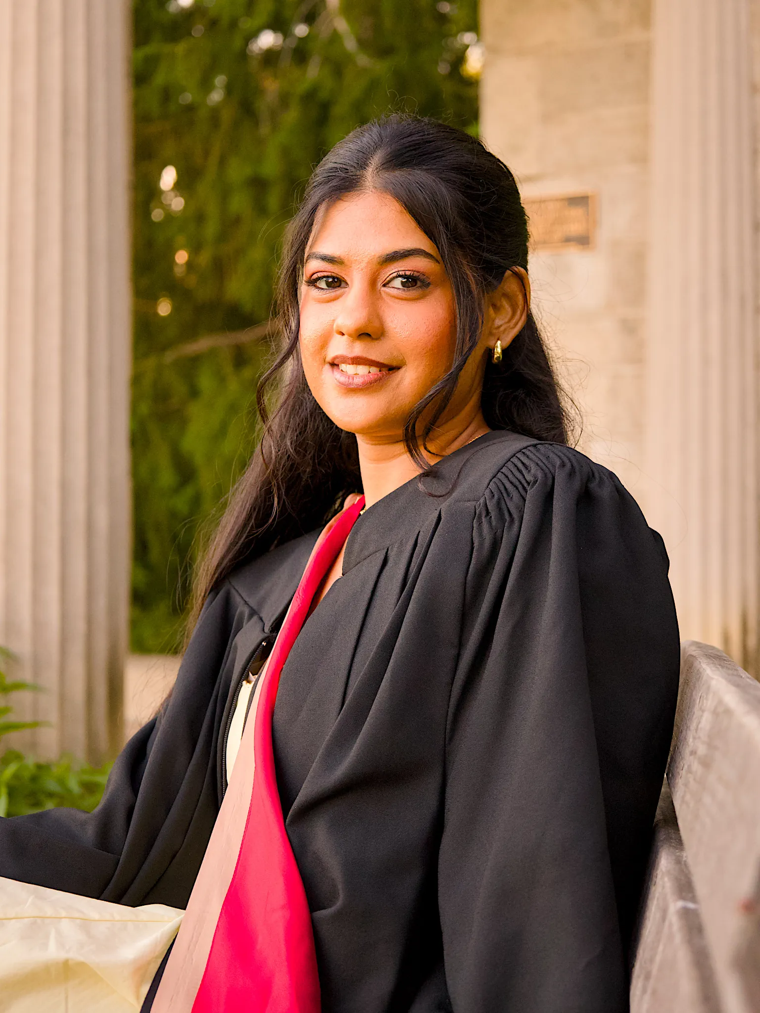 A University of Guelph graduate in regalia beside the stone colonnade.