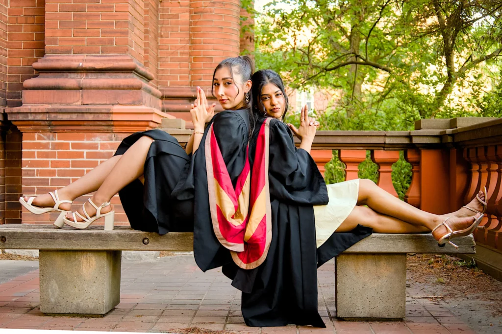 Two University of Guelph graduates together on the bench outside the red-brick hall.