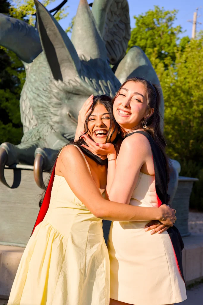 Two University of Guelph graduates hugging at the bronze Gryphon statue.
