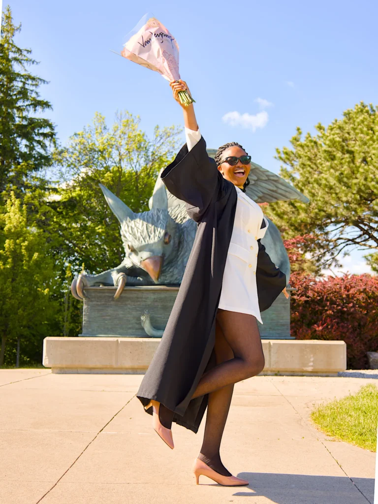 A University of Guelph graduate in regalia raising her bouquet by the bronze Gryphon statue.