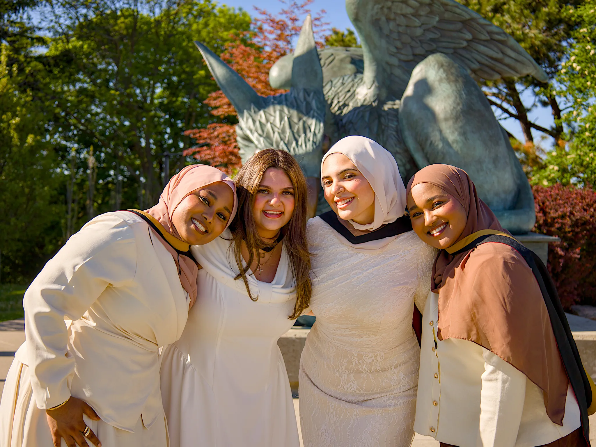 Four University of Guelph graduates hugging by the bronze Gryphon statue.