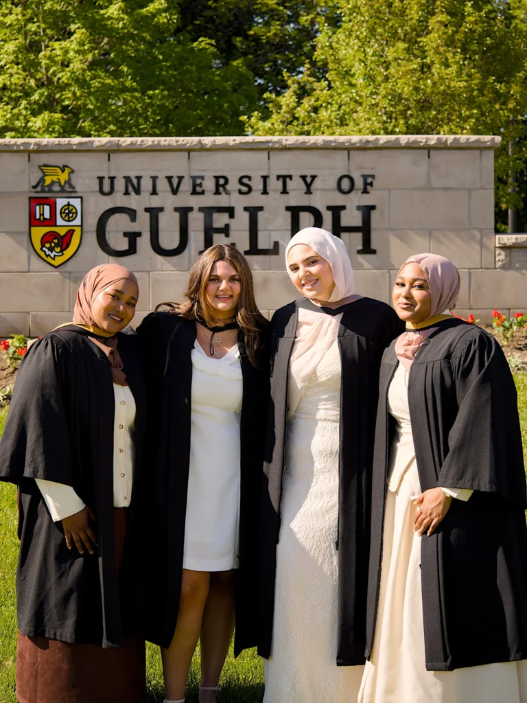 Four University of Guelph graduates together at the University of Guelph entrance sign.