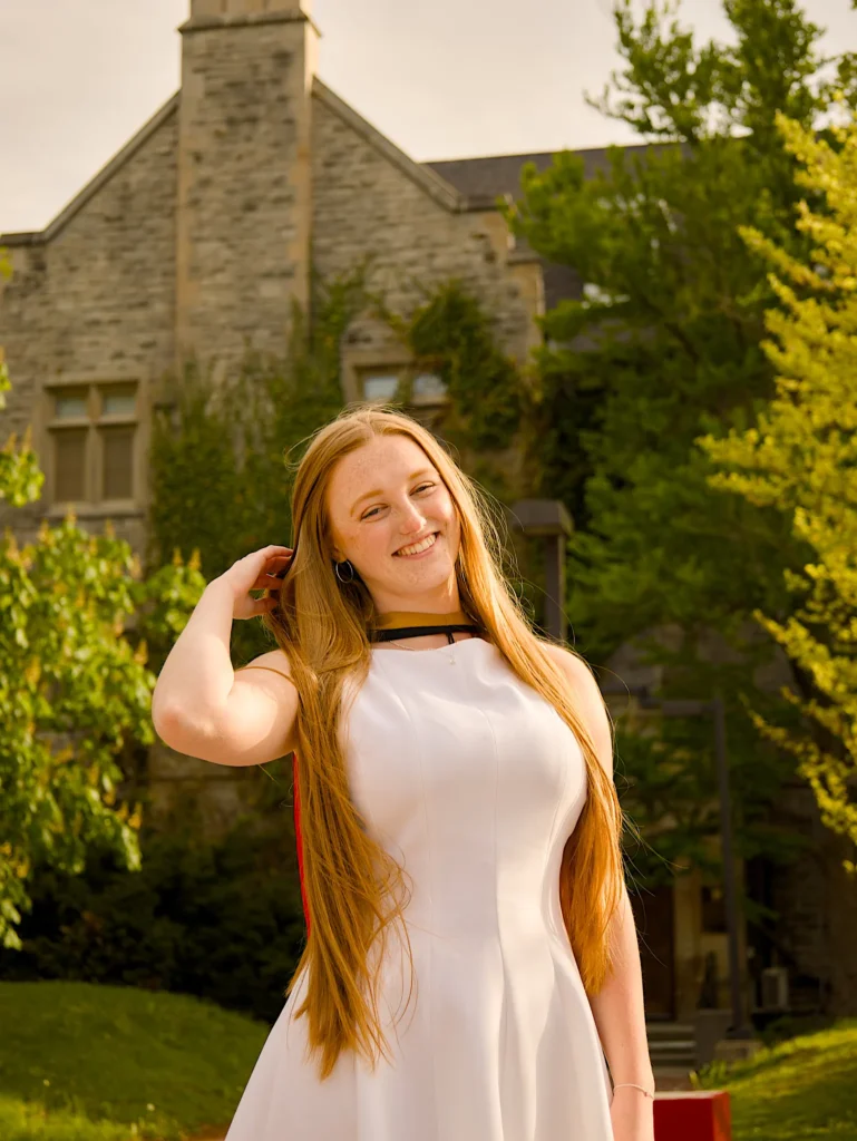 A University of Guelph graduate in regalia beside a limestone campus building.