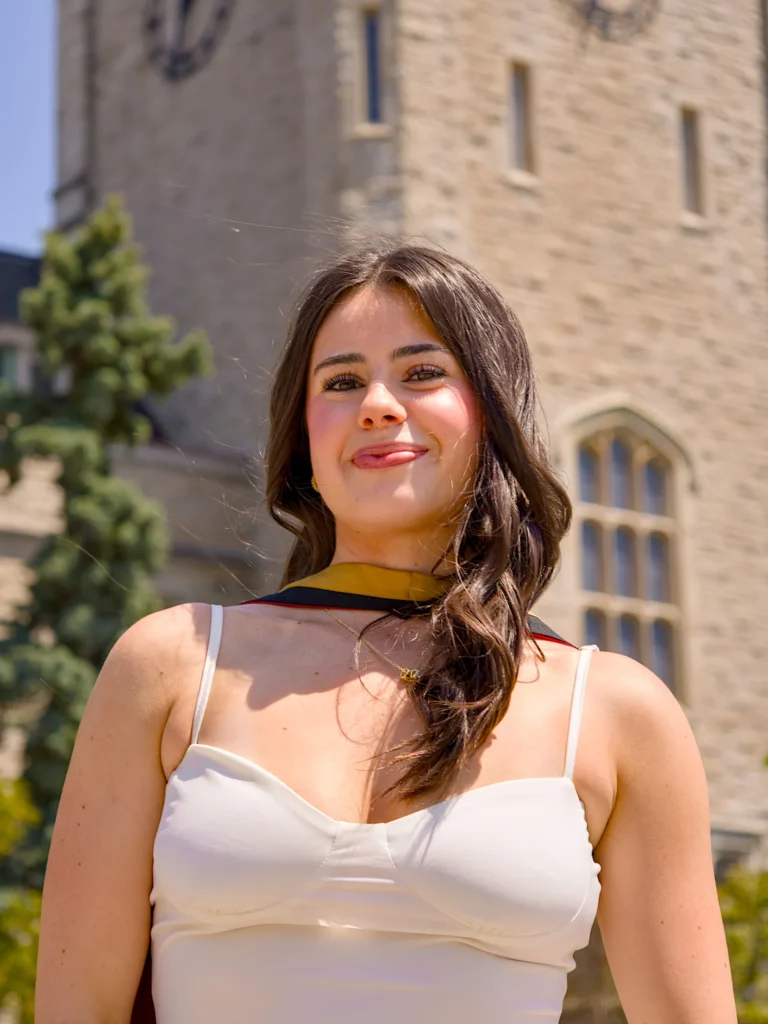 A University of Guelph graduate in regalia with the limestone Johnston Hall tower behind.