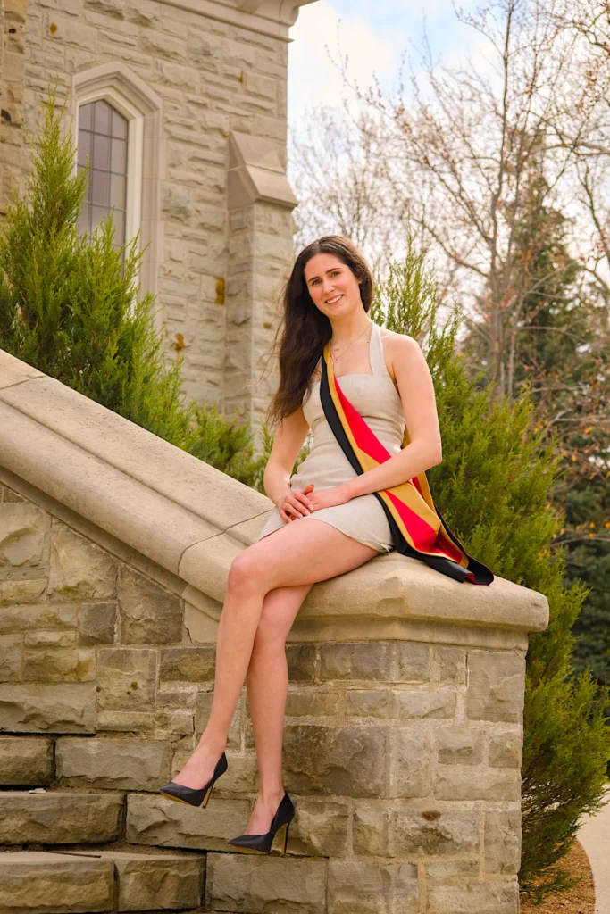 A University of Guelph graduate in regalia sitting on the limestone steps.
