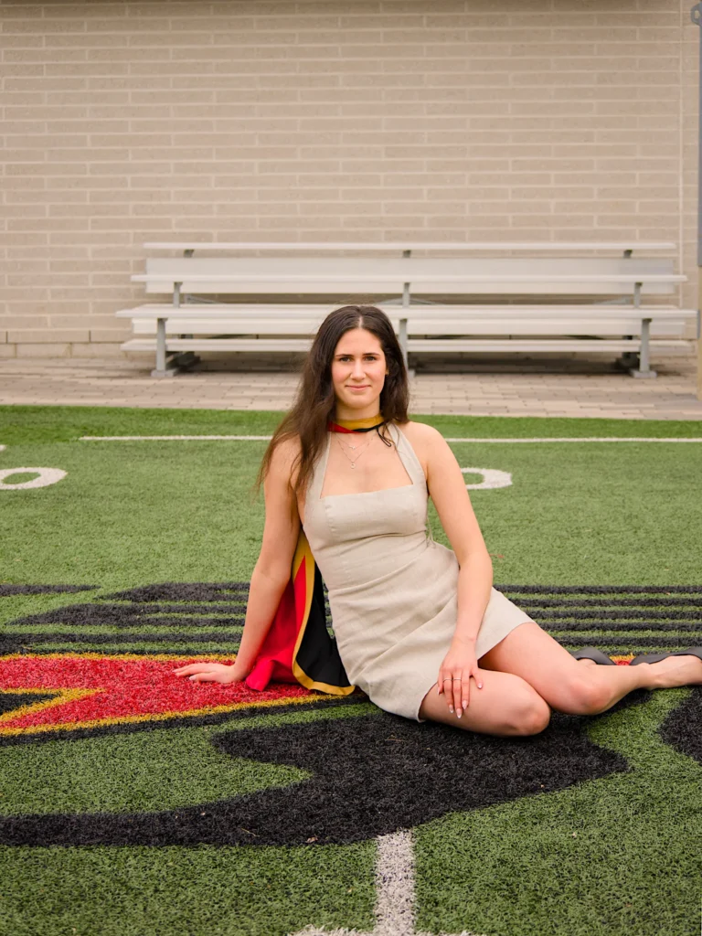 A University of Guelph graduate in regalia sitting on the Gryphons logo at Alumni Stadium.